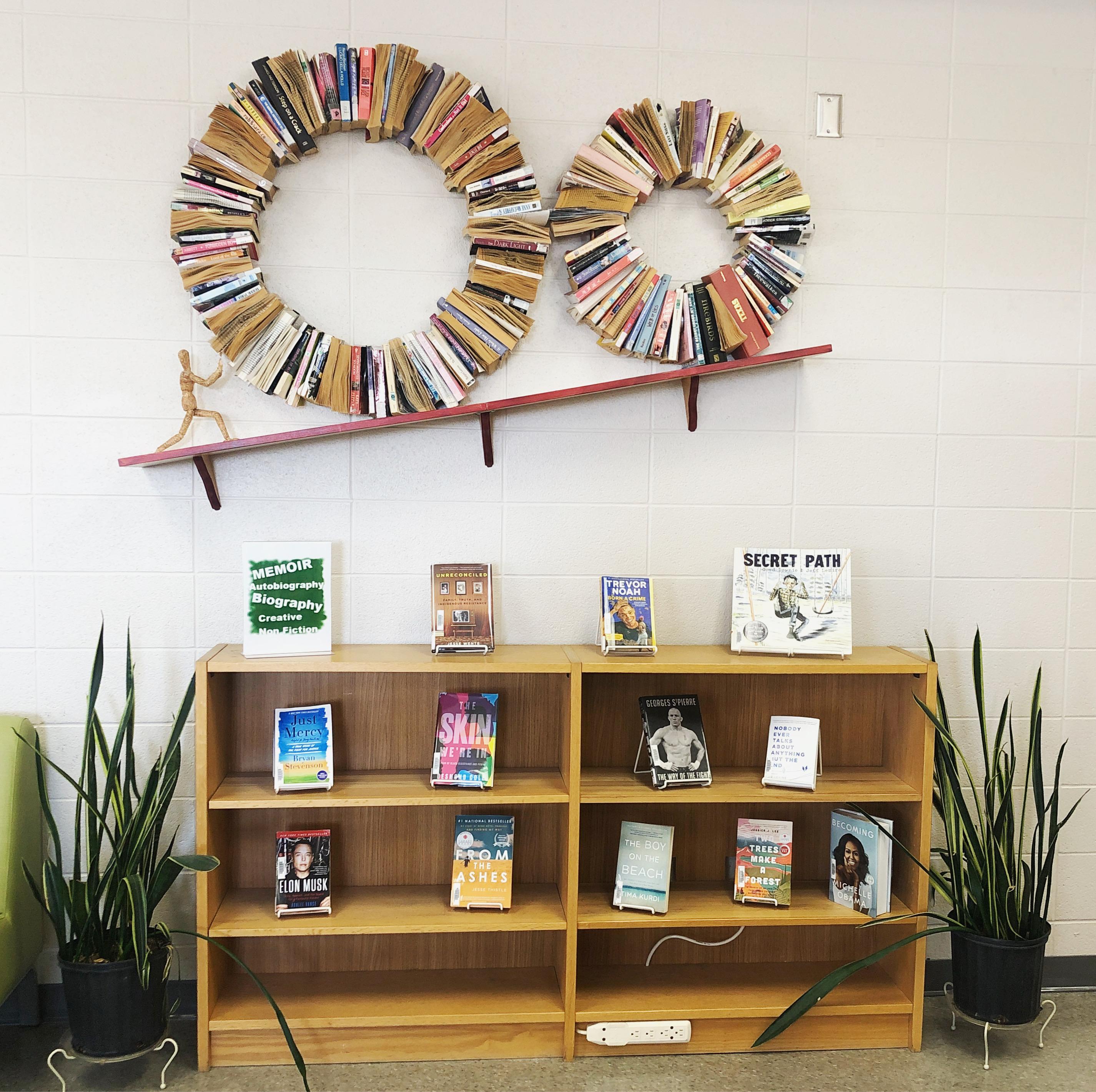 bookshelf on floor with books on display. A crooked shelf above displays books in circular shape